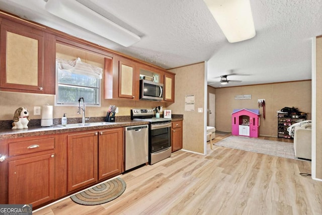 kitchen with brown cabinetry, a textured ceiling, appliances with stainless steel finishes, light wood-type flooring, and a sink