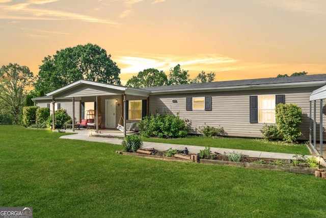 back of house at dusk with a lawn, covered porch, and a carport