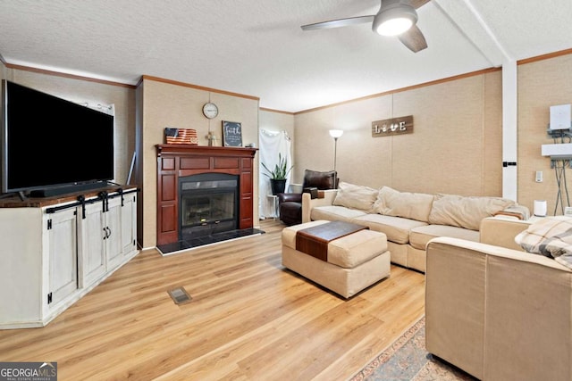 living room with a textured ceiling, light wood-style flooring, a ceiling fan, visible vents, and ornamental molding