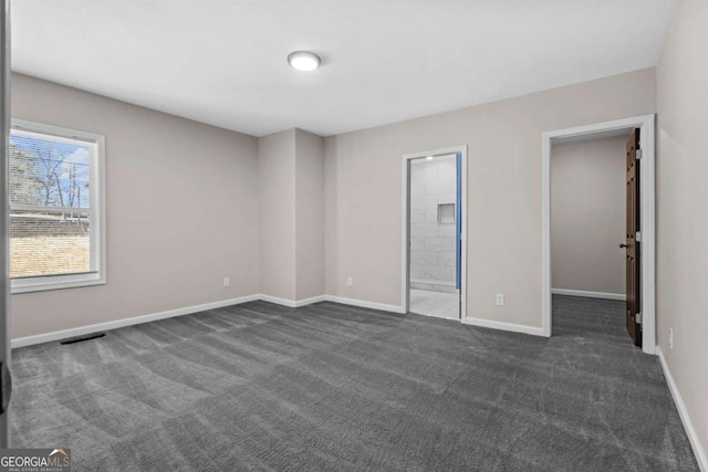 unfurnished bedroom featuring visible vents, baseboards, a spacious closet, ensuite bathroom, and dark carpet