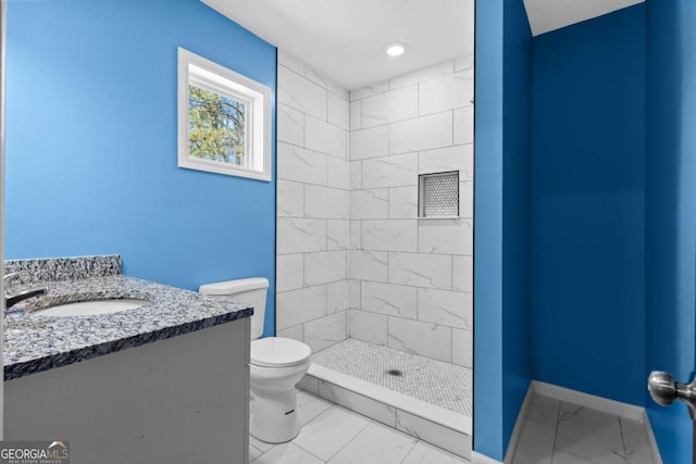 bathroom with a tile shower, vanity, toilet, marble finish floor, and baseboards