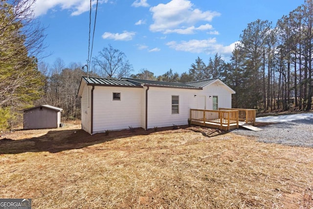 rear view of house with a storage shed, a wooden deck, a standing seam roof, an outdoor structure, and metal roof