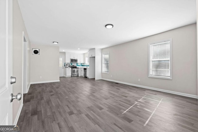 unfurnished living room with dark wood-style flooring and baseboards