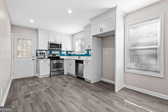 kitchen featuring wood finished floors, baseboards, plenty of natural light, white cabinets, and appliances with stainless steel finishes