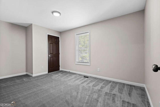 spare room with baseboards, dark carpet, and visible vents