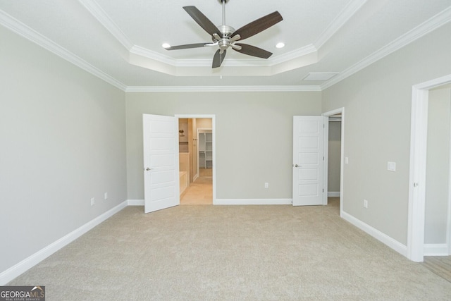 unfurnished bedroom with ornamental molding, light carpet, baseboards, a walk in closet, and a tray ceiling