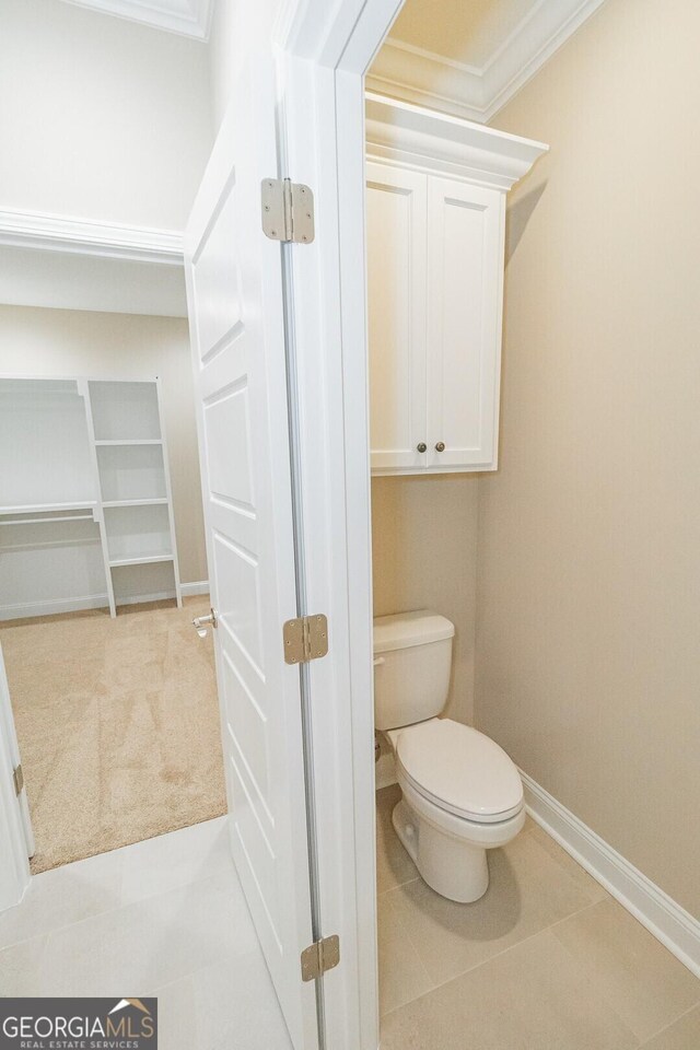 bathroom with baseboards, crown molding, tile patterned floors, and toilet