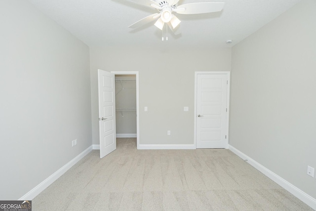 unfurnished bedroom with a closet, baseboards, a walk in closet, ceiling fan, and carpet