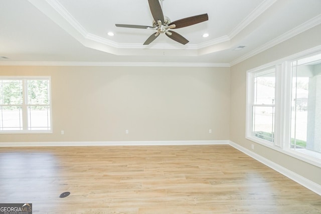 empty room with a ceiling fan, visible vents, a raised ceiling, light wood finished floors, and ornamental molding