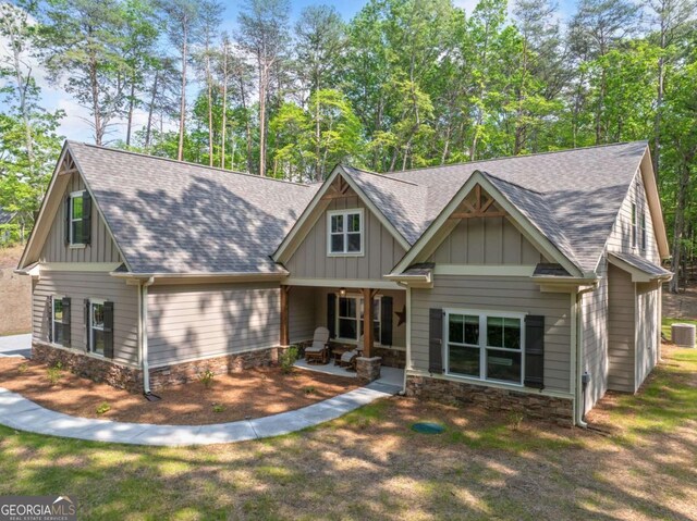 craftsman-style house featuring roof with shingles, board and batten siding, cooling unit, and stone siding