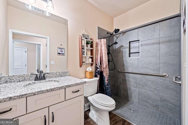 full bathroom featuring tiled shower, vanity, toilet, and wood finished floors