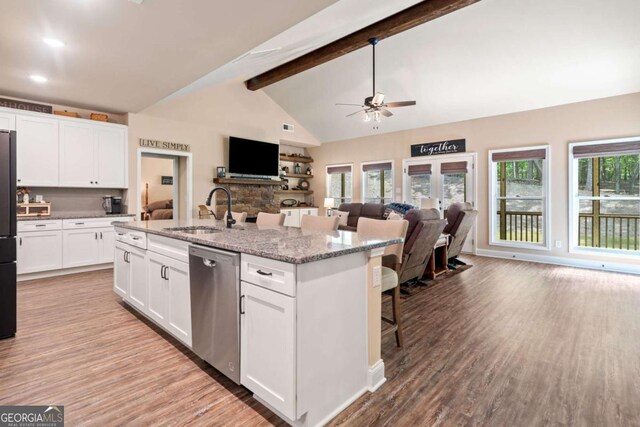 kitchen featuring stainless steel dishwasher, a ceiling fan, open floor plan, a sink, and light wood finished floors