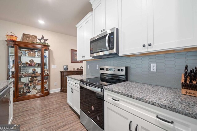 kitchen featuring appliances with stainless steel finishes, tasteful backsplash, light wood-type flooring, light stone counters, and white cabinetry