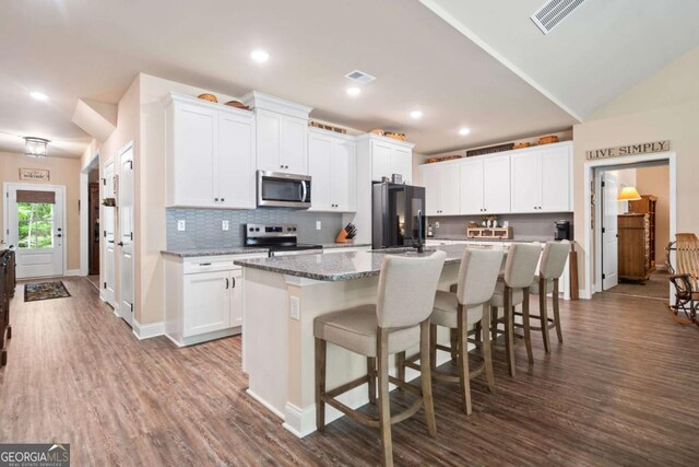 kitchen featuring a breakfast bar area, an island with sink, stainless steel appliances, dark wood-type flooring, and visible vents