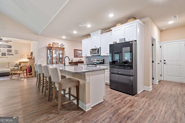 kitchen with appliances with stainless steel finishes, a breakfast bar, an island with sink, white cabinetry, and wood finished floors