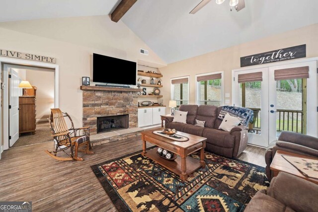 living area featuring visible vents, wood finished floors, beam ceiling, a stone fireplace, and ceiling fan