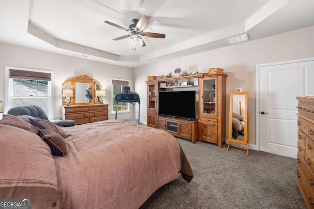 bedroom featuring visible vents, a ceiling fan, a tray ceiling, and light colored carpet