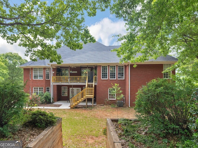rear view of house featuring a patio, a lawn, a shingled roof, brick siding, and stairs