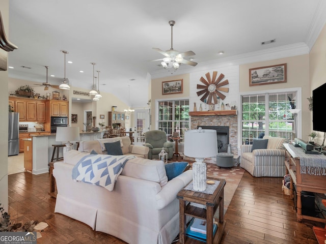 living area with ceiling fan with notable chandelier, wood-type flooring, a fireplace, crown molding, and visible vents