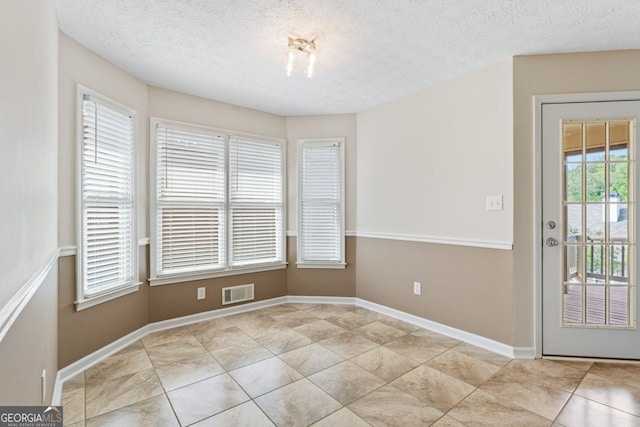 unfurnished dining area featuring baseboards, a textured ceiling, visible vents, and light tile patterned floors