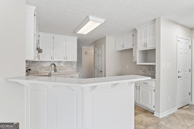 kitchen featuring decorative backsplash, a peninsula, light countertops, a textured ceiling, and white cabinets