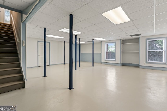 basement with stairs, baseboards, a drop ceiling, and a healthy amount of sunlight