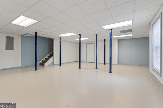 basement with a paneled ceiling, stairway, and electric panel