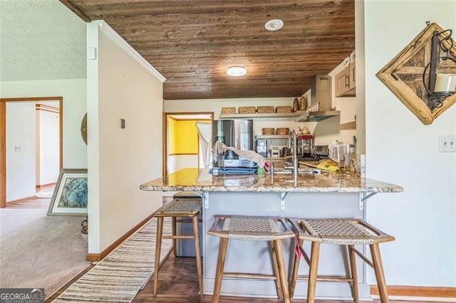 kitchen featuring a peninsula, wood ceiling, a kitchen bar, and light stone counters
