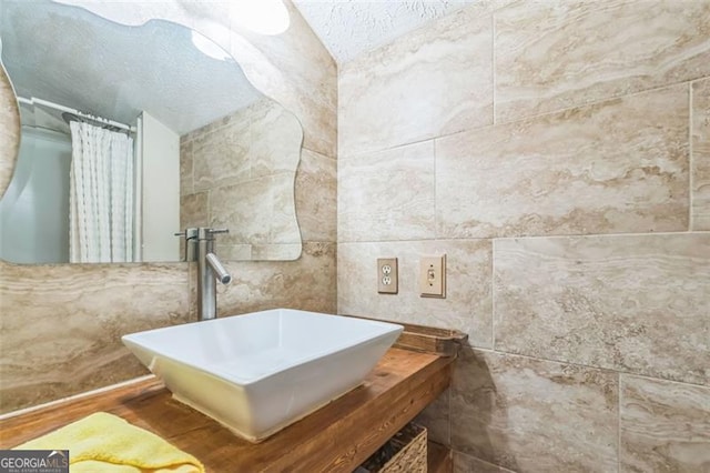 full bath with a textured ceiling, a shower with curtain, tile walls, and a sink