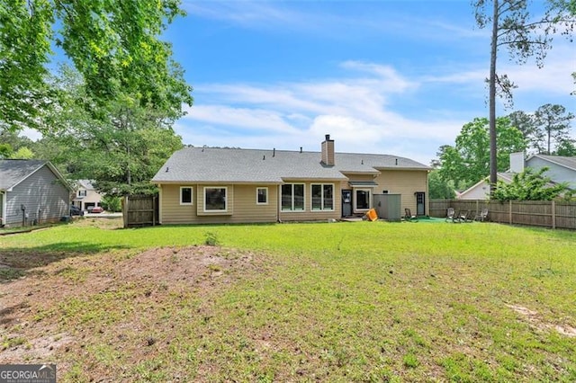 rear view of house featuring fence, a yard, and a chimney