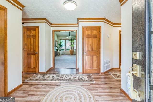 foyer entrance featuring visible vents, ornamental molding, wood finished floors, baseboards, and a textured ceiling
