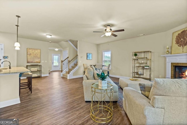 living room with dark wood finished floors, stairs, a ceiling fan, baseboards, and a tile fireplace