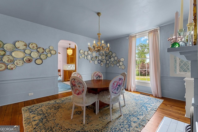 dining room with an inviting chandelier, wainscoting, arched walkways, visible vents, and hardwood / wood-style flooring