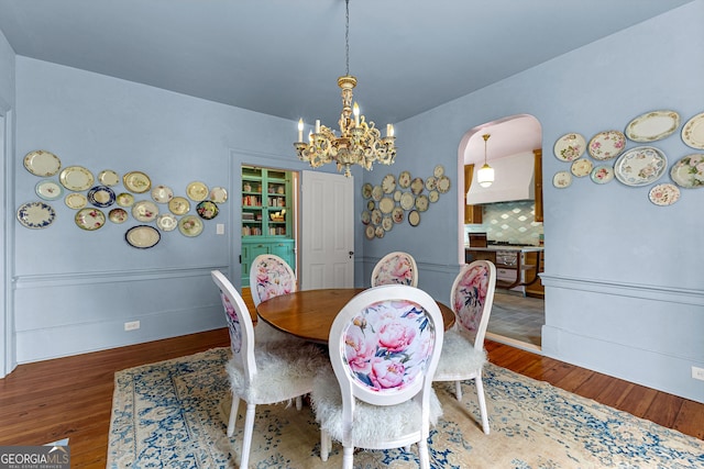 dining space featuring arched walkways, baseboards, wood finished floors, and a notable chandelier