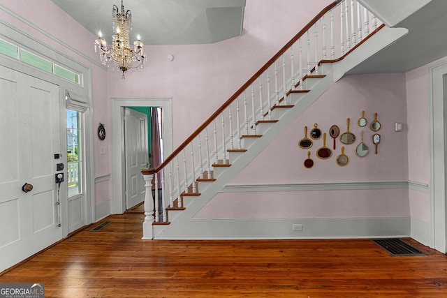foyer entrance with an inviting chandelier, wood-type flooring, stairs, and visible vents