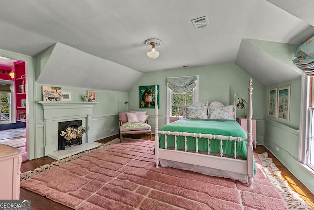 bedroom featuring visible vents, a decorative wall, lofted ceiling, wood finished floors, and a fireplace
