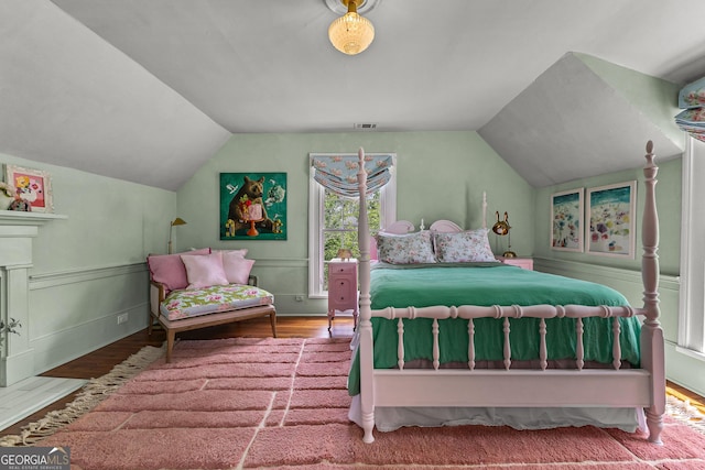 bedroom featuring visible vents, a decorative wall, wood finished floors, and lofted ceiling