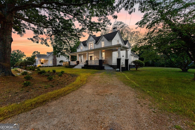 view of front facade featuring a front yard, driveway, covered porch, and a chimney