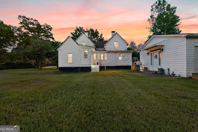 rear view of house featuring entry steps, a chimney, and a yard
