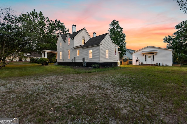 back of property at dusk featuring a lawn and a chimney