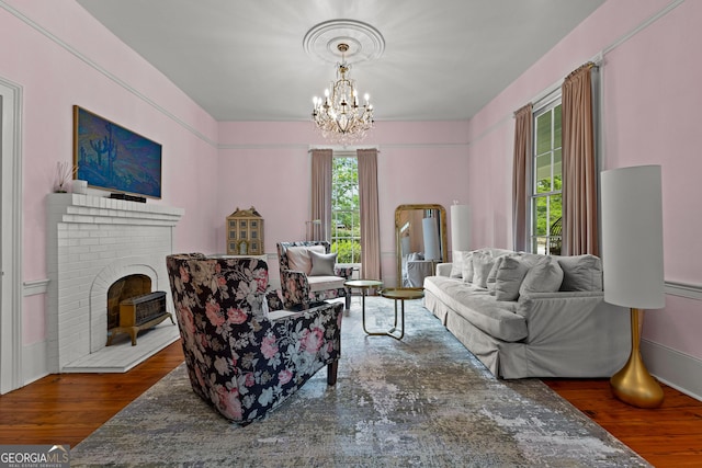 living room featuring an inviting chandelier, a brick fireplace, and wood finished floors
