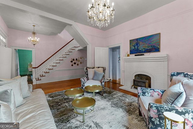 living area with an inviting chandelier, a fireplace, stairs, and wood finished floors
