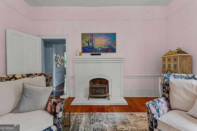 living area featuring baseboards, a brick fireplace, and wood finished floors