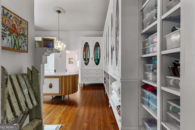 walk in closet with dark wood-type flooring and a notable chandelier