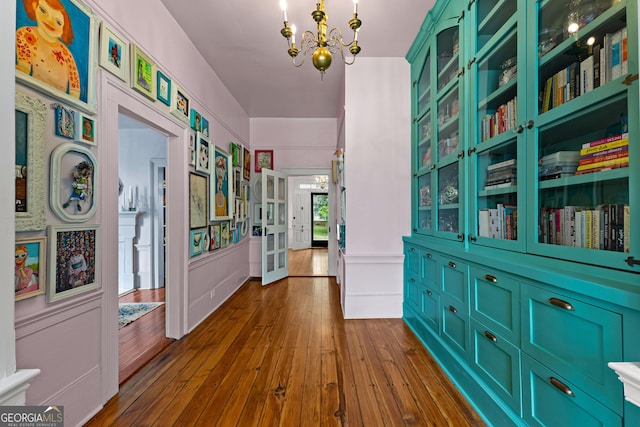 hall featuring a wainscoted wall, a decorative wall, dark wood-style floors, and a notable chandelier