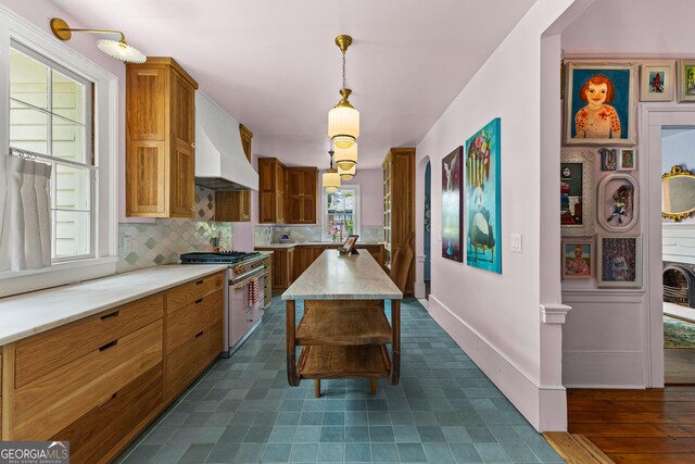 kitchen featuring decorative light fixtures, high end stove, tasteful backsplash, brown cabinets, and premium range hood