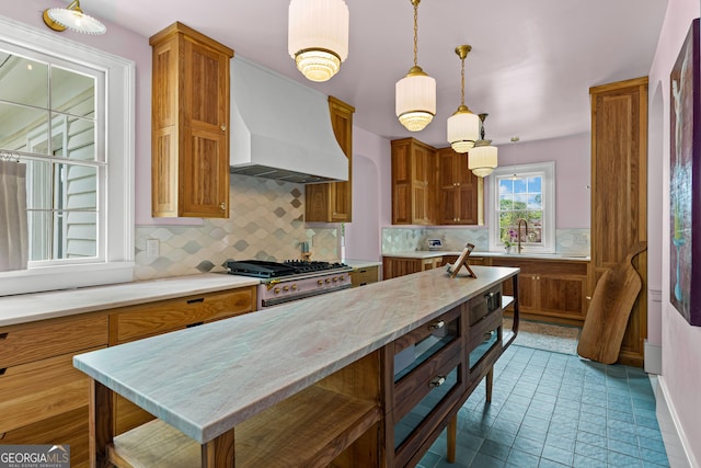kitchen with brown cabinetry, premium range hood, decorative light fixtures, and tasteful backsplash