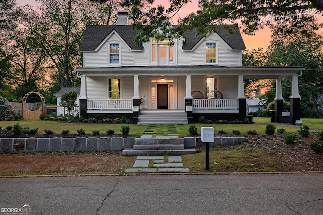 modern farmhouse style home featuring roof with shingles, a yard, covered porch, and a chimney