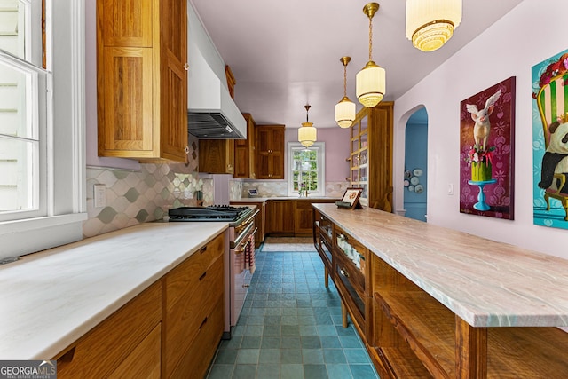 kitchen with gas range, brown cabinets, tasteful backsplash, custom range hood, and arched walkways