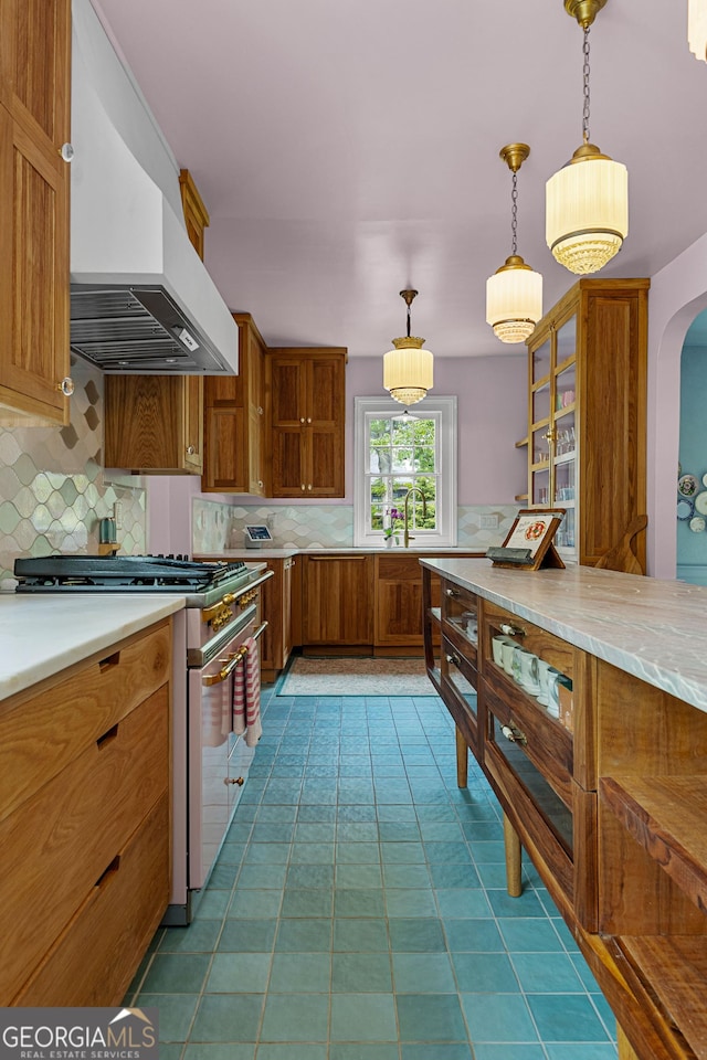 kitchen with brown cabinetry, tasteful backsplash, light countertops, premium range hood, and range with gas stovetop